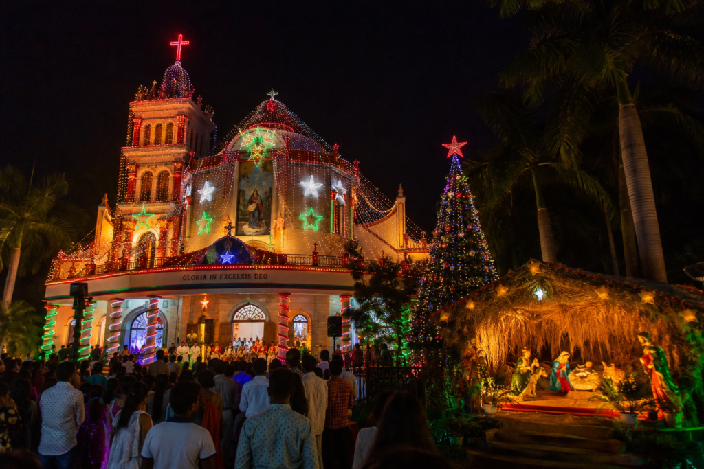 A beautifully illuminated church decorated with colorful Christmas lights, a Christmas tree, and a nativity scene as people gather to celebrate Christmas in Telangana.